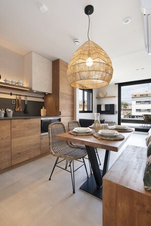 A modern kitchen with wooden cabinets, a dining area with wicker chairs, and a large woven pendant light.