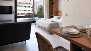A modern hotel room with a bed, a sofa, a dining table, and a TV. - Apartamentos Balisse (Castelldefels)