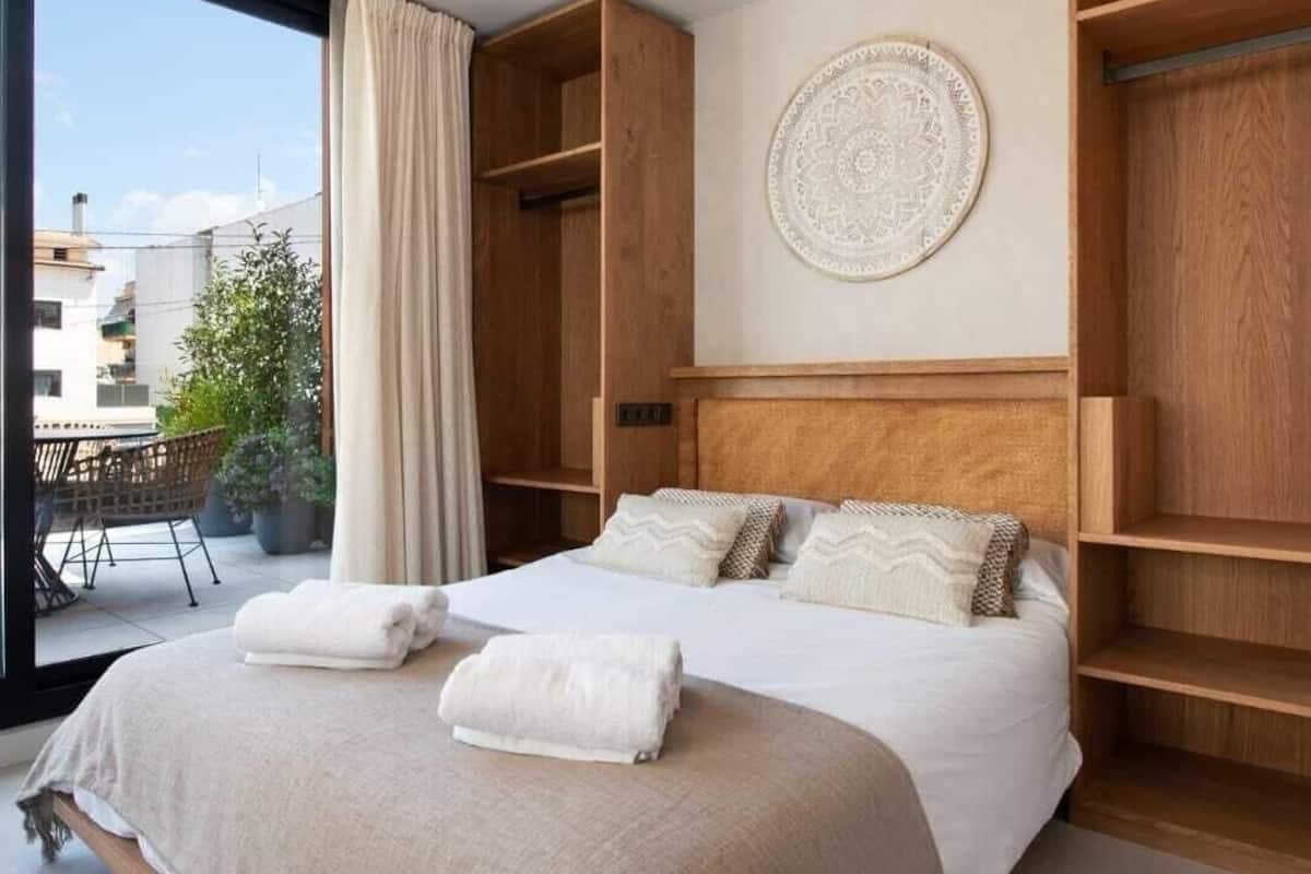 A bedroom with a large bed, built-in wooden shelving, a circular wall decoration, and a view through a large window.
