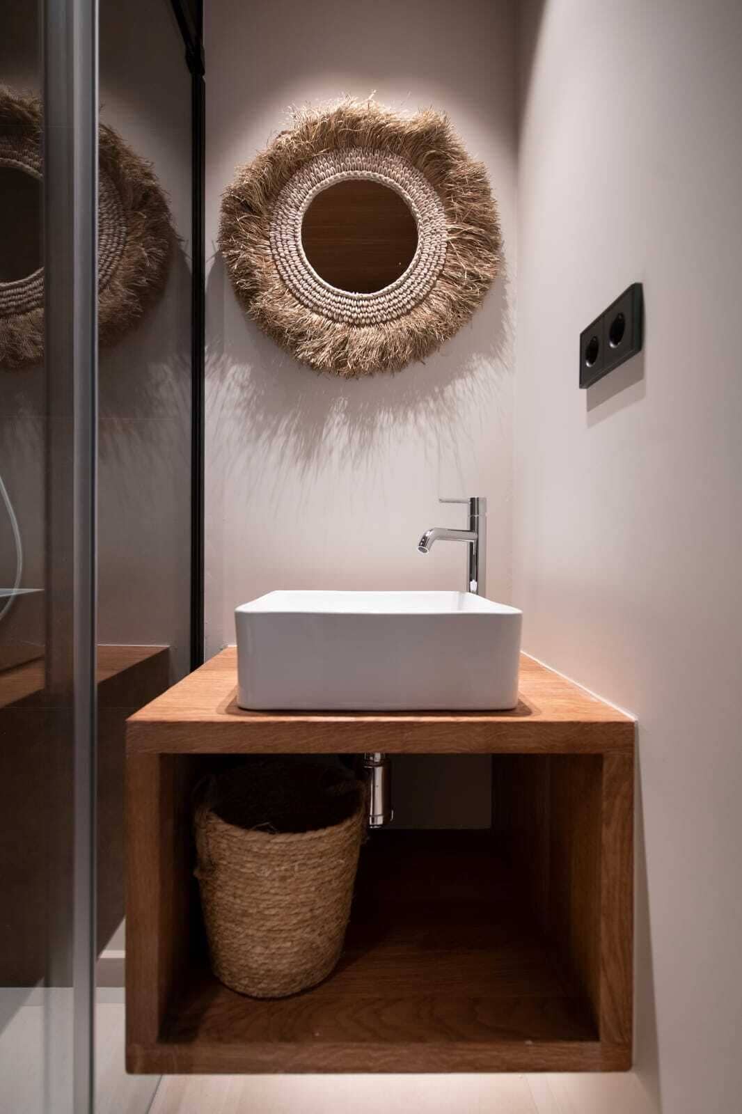 Un baño moderno con un lavamanos blanco, tocador de madera y un adorno de pared tejido.