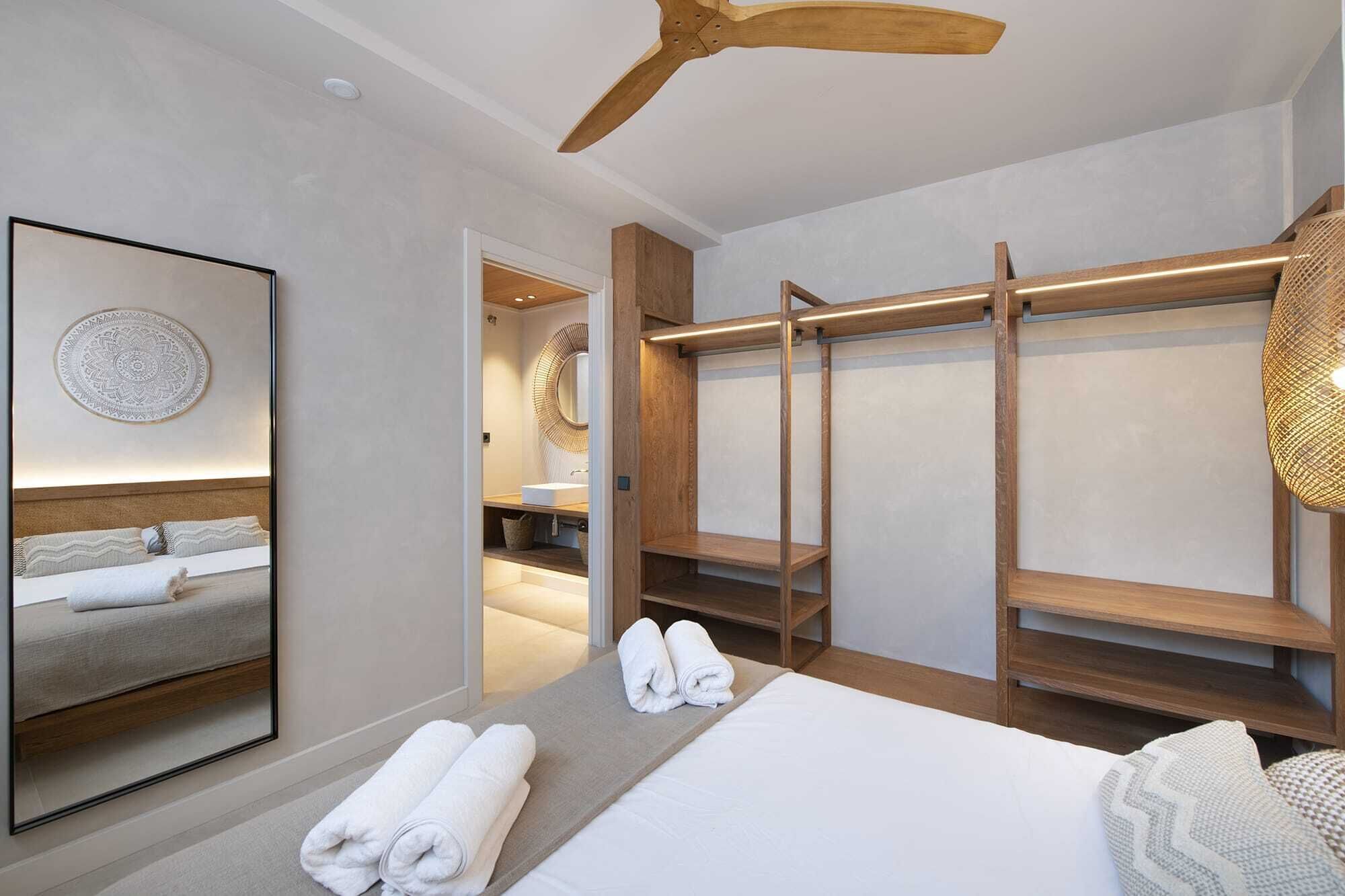 Ein modernes Hotelzimmer mit einem Bett, einem großen Spiegel, einem Holzschrank und einem Deckenventilator.