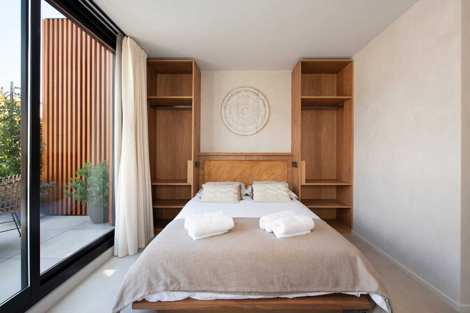 Une chambre à coucher avec un lit, une grande fenêtre, une plante en pot et un panneau mural en bois.