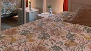 Een slaapkamer met een bed, nachtkastje, spiegel en raam met gordijnen.