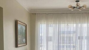 Een woonkamer met een bank, een lijst met foto aan de muur en een groot raam met transparante gordijnen.
