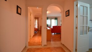 A hallway leading to a living area with a red sofa, a dining table, and a kitchen area visible through an open door. - LAS DUNAS 51 - Three Bedroom Apartment, Sleeps 7 (Punta del moral)
