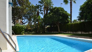 Uma piscina azul cristalina com borda azulejada, rodeada por vegetação exuberante e palmeiras.