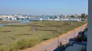 Uma marina costeira com barcos atracados, uma praia de areia e uma estrada com calçada.