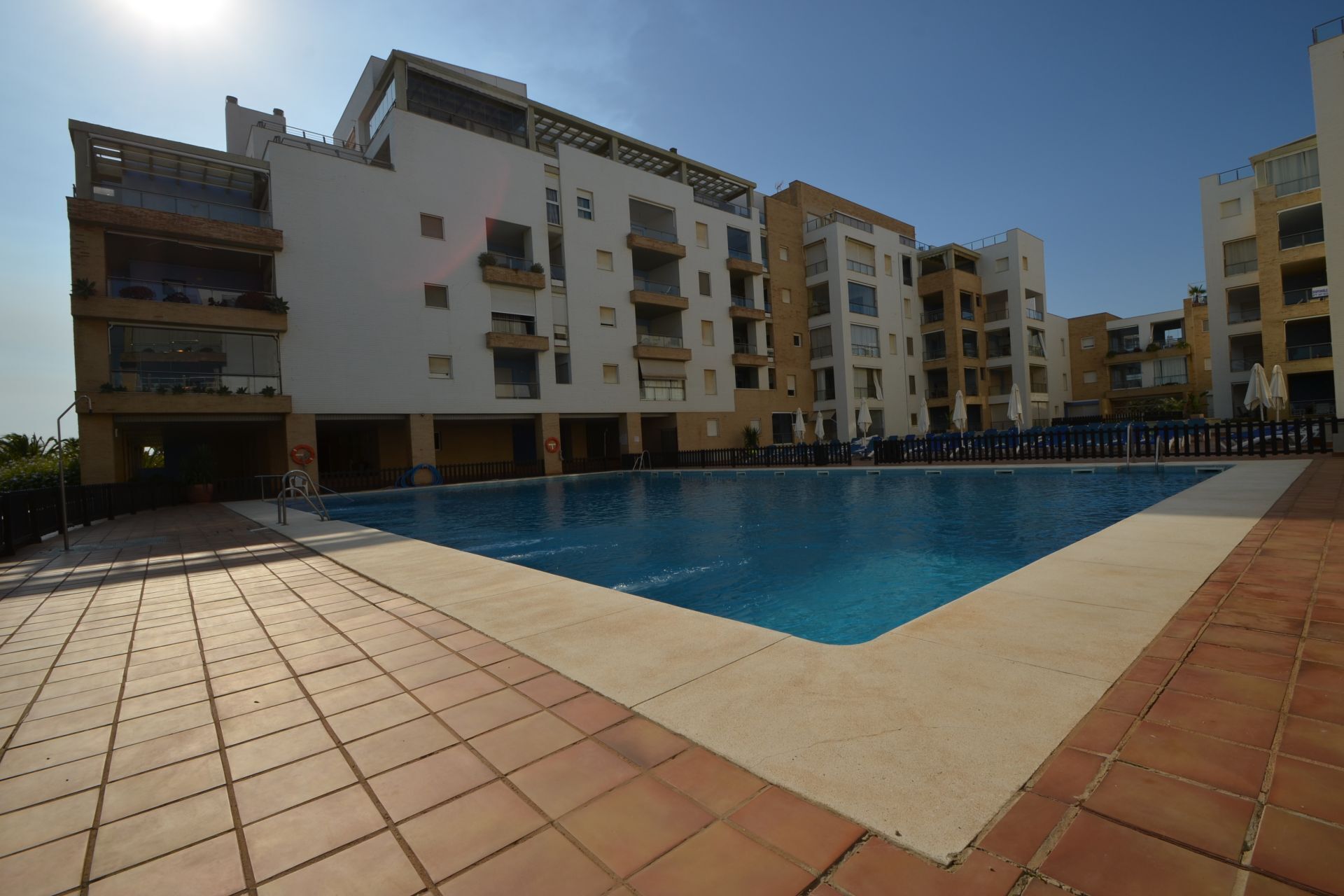 Une piscine entourée d’immeubles résidentiels à plusieurs étages, dotés de balcons et d’une allée dallée.