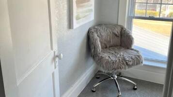 Una habitación con alfombra gris, una butaca gris y mullida, una puerta blanca y un ventanal con vistas a una carretera y árboles.