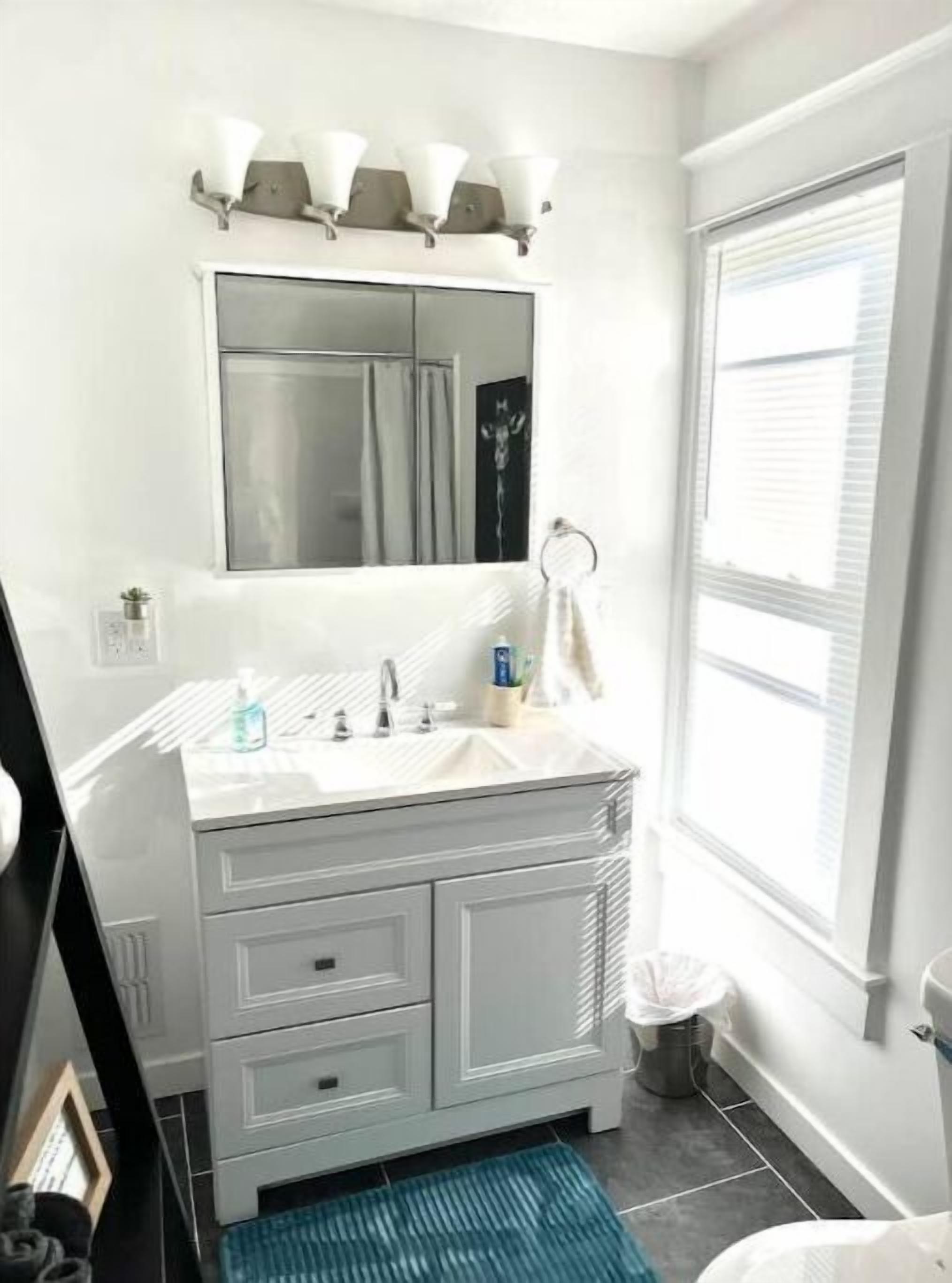 Un baño con un tocador blanco, un espejo y una ventana.