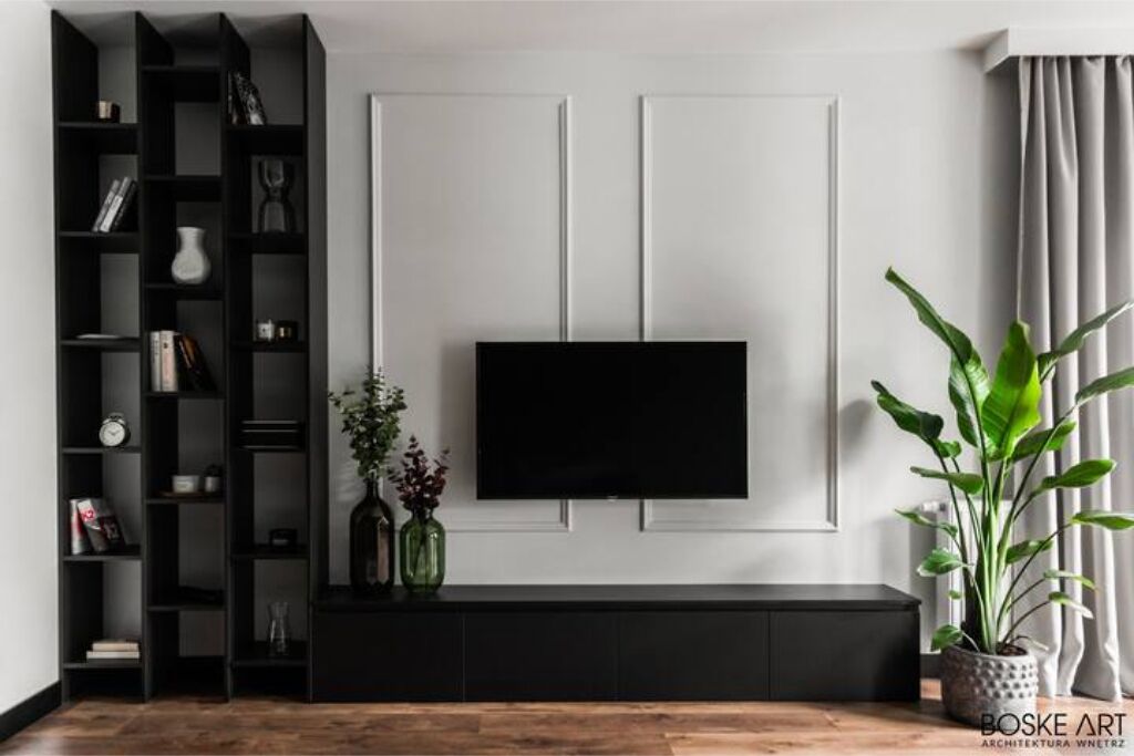 A modern living room with a black entertainment unit, a flat-screen TV mounted on the wall, and a potted plant on the right.