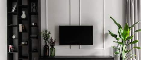 Una sala de estar moderna con un mueble de entretenimiento negro, un televisor de pantalla plana montado en la pared y una planta en maceta a la derecha.
