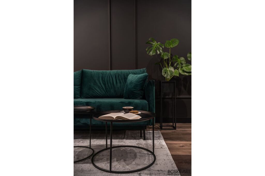 A modern living room with a teal sofa, a round coffee table with an open book, and a potted plant.