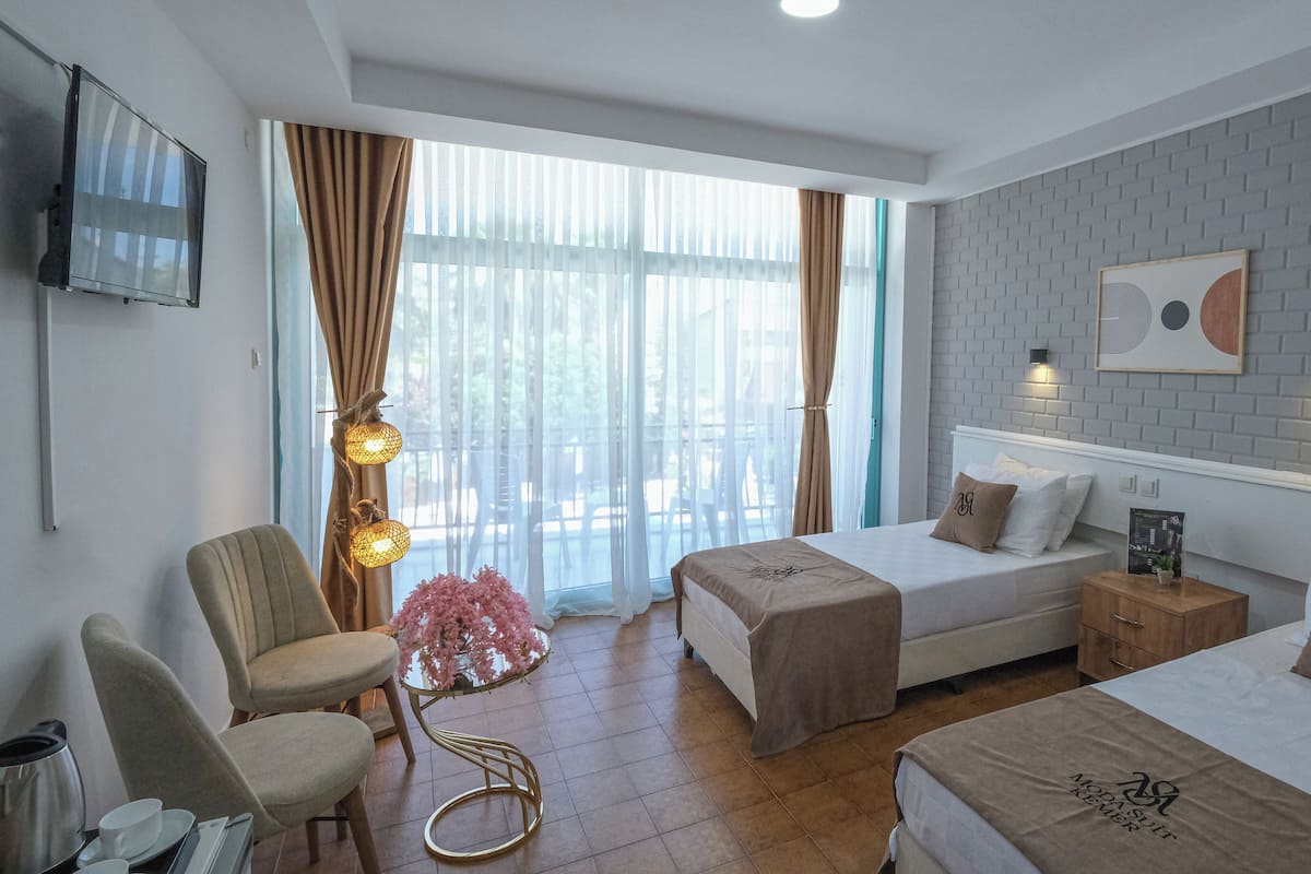 Habitación de hotel con dos camas, televisión, escritorio con silla y ventana con cortinas.