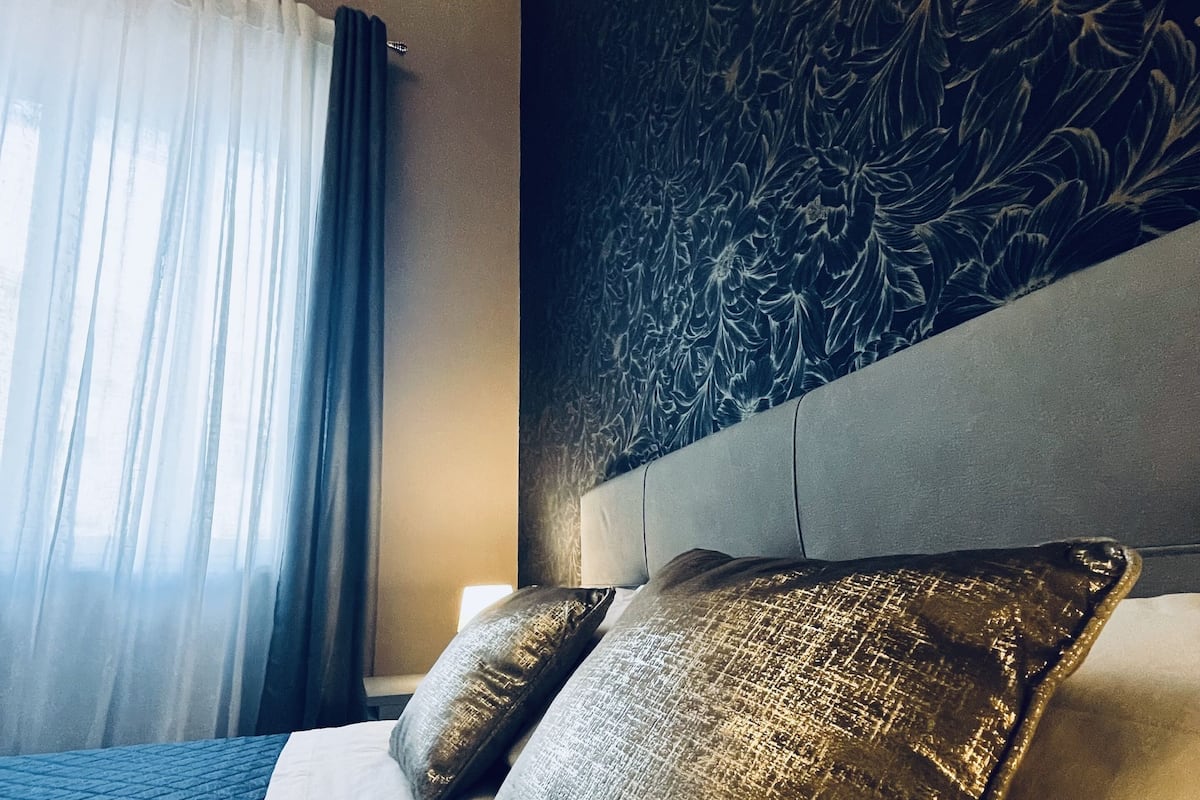 Ein Hotelzimmer mit einem großen Bett, einem Blumenmuster an der Kopfteil und durchsichtigen Vorhängen.