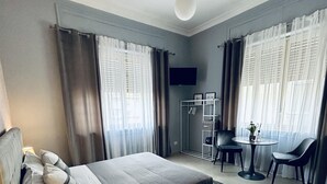 Habitación de hotel moderna con una cama grande, un escritorio y una silla. Hay un televisor en la pared y una pequeña mesa con una planta.
