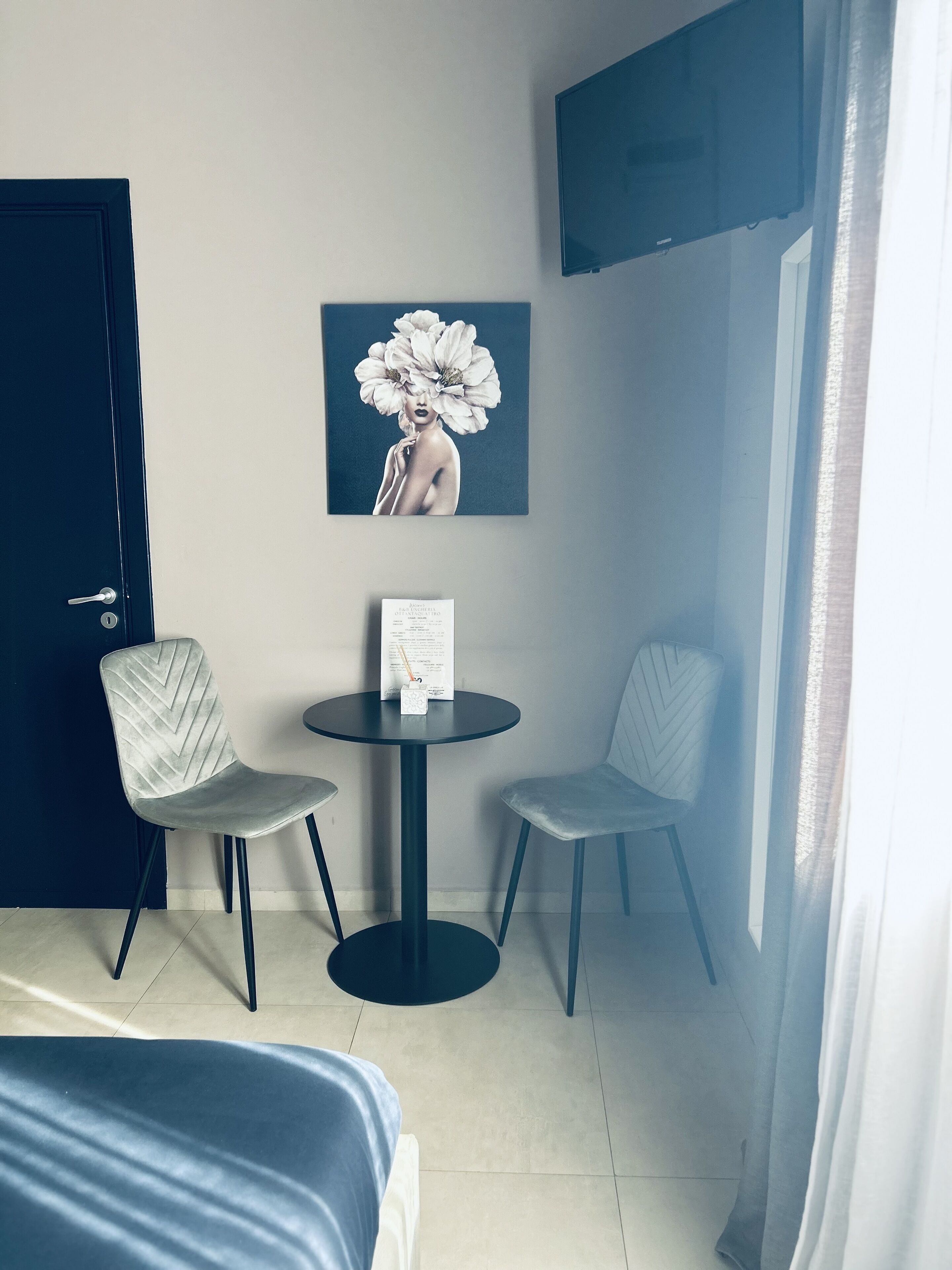A hotel room with a bed, a small round table with two chairs, a painting on the wall, and a TV mounted above the table.