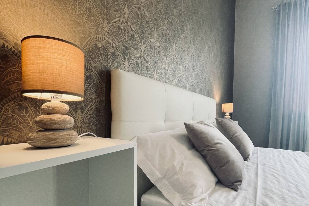 Ein modernes Schlafzimmer mit weißem Kopfteil, einem Nachttisch mit Lampe und einer eingebauten Ablage mit einem Buch.