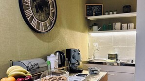 Una cocina con un reloj de pared grande, una cafetera, una cesta de frutas y un pastel en la encimera.