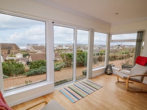 A spacious room with large windows offering a view of a residential area and the sea. - Strandview (Coleraine)