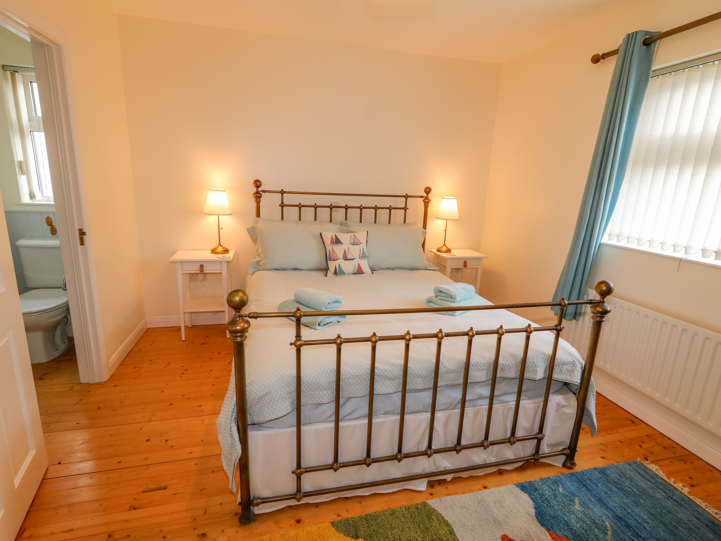 Une chambre à coucher avec un lit en bois, deux tables de chevet avec des lampes, une fenêtre avec des rideaux et un radiateur.