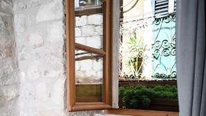 A small kitchen with a wooden stool, a white countertop, and a window with a view of a green gate and plants. - Live Laugh Love Dubrovnik luxury rooms (Dubrovnik)