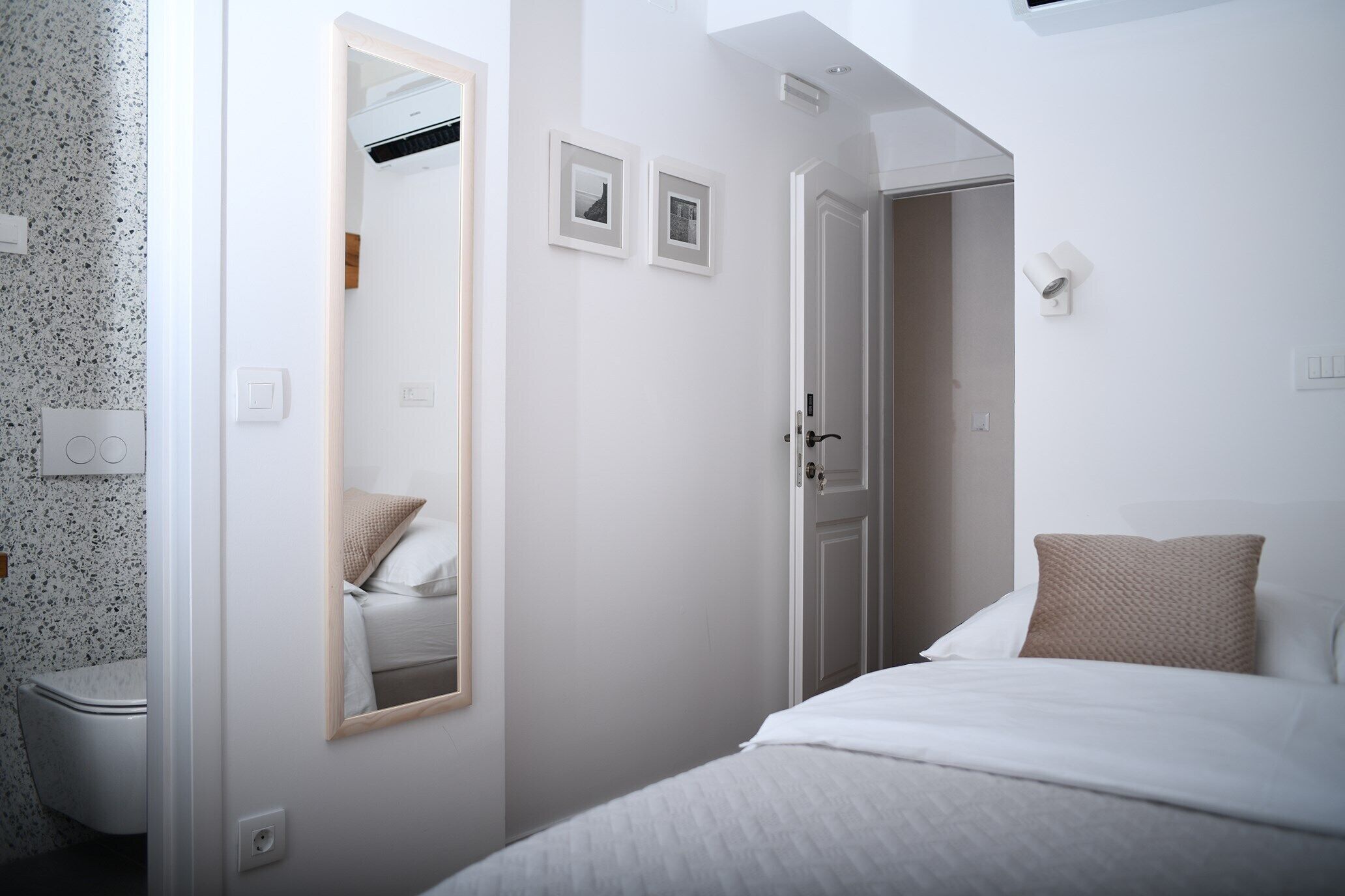 Un dormitorio con cama, espejo, puerta y lámpara fijada a la pared.