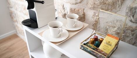 Une table préparée pour le petit-déjeuner avec une machine à café, deux tasses blanches, un plateau et une boîte de thé Twinings.