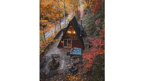 A cabin with a sloped roof, a wooden deck, and a hot tub.