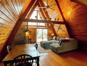 A cozy attic room with wooden walls and a sloped ceiling. There is a dining table with chairs, a sofa, and a small table with a lamp. - The Lodge at Ski Mountain (Gatlinburg)