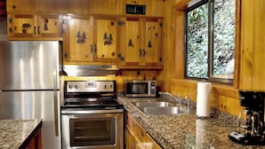 A kitchen with wooden cabinets, stainless steel appliances, granite countertops, and a window with a forest view.