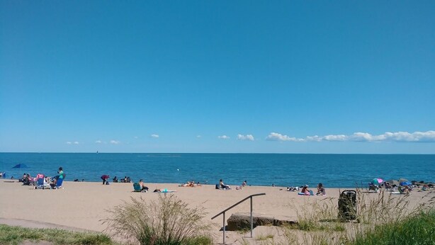 A beach with people sunbathing and swimming, a clear sky, and a calm sea. - The Gorgeous George Beach Cottage (East Haven)