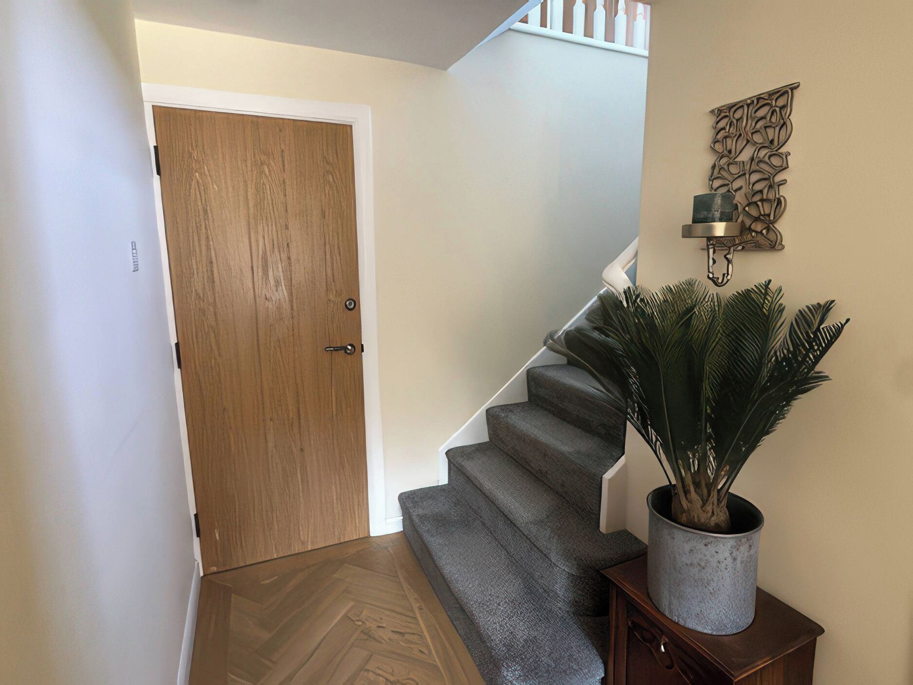 Eine Holztür, eine Treppe mit Teppichstufen, ein Blumentopf und eine wandmontierte Leuchte.