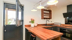 Une cuisine moderne avec un plan de travail en bois, un évier noir et un four encastré. Il y a une fenêtre donnant sur l’extérieur et une porte avec une poignée.