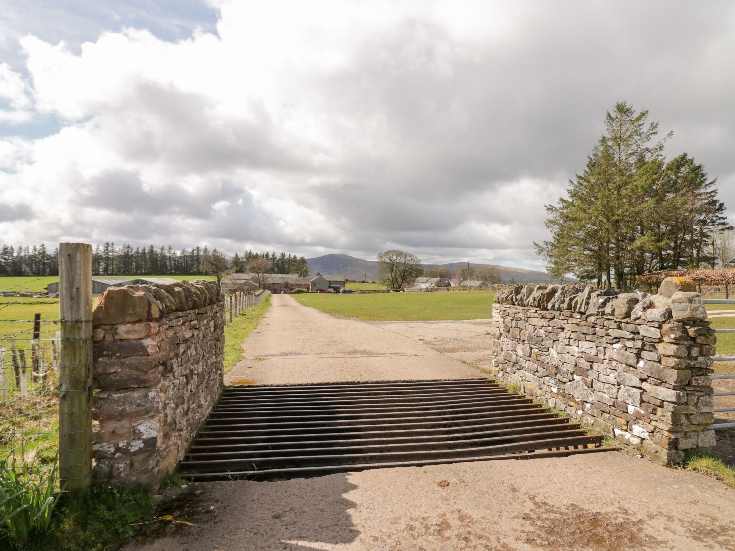 A rural pathway leading to a stone gate, surrounded by fields and trees.