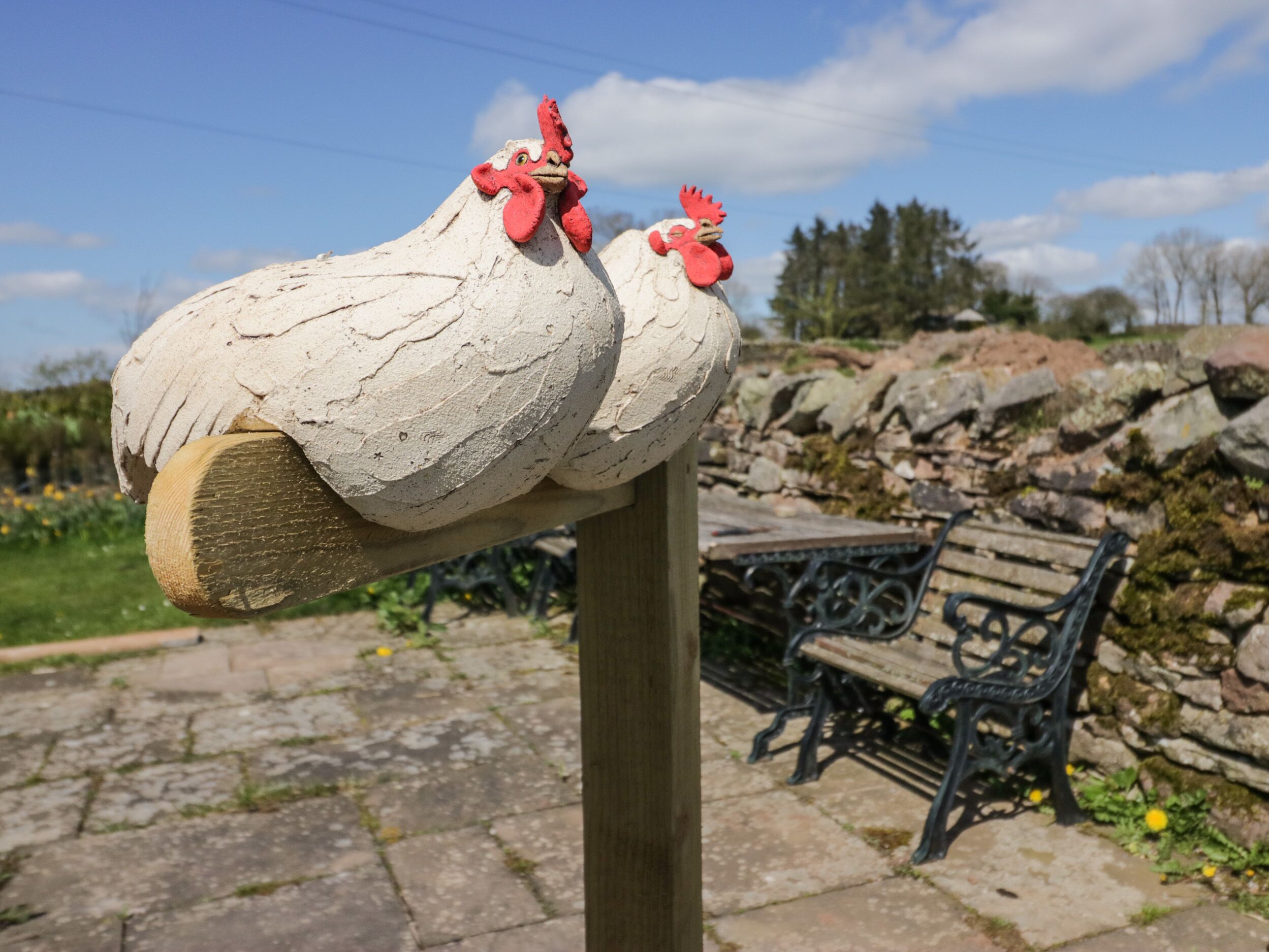 Een beeldhouwwerk van twee kippen bevestigd aan een houten paal.