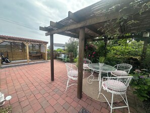 Un espace patio agrémenté d’une pergola, de meubles pour s’asseoir à l’extérieur et d’un jardin.