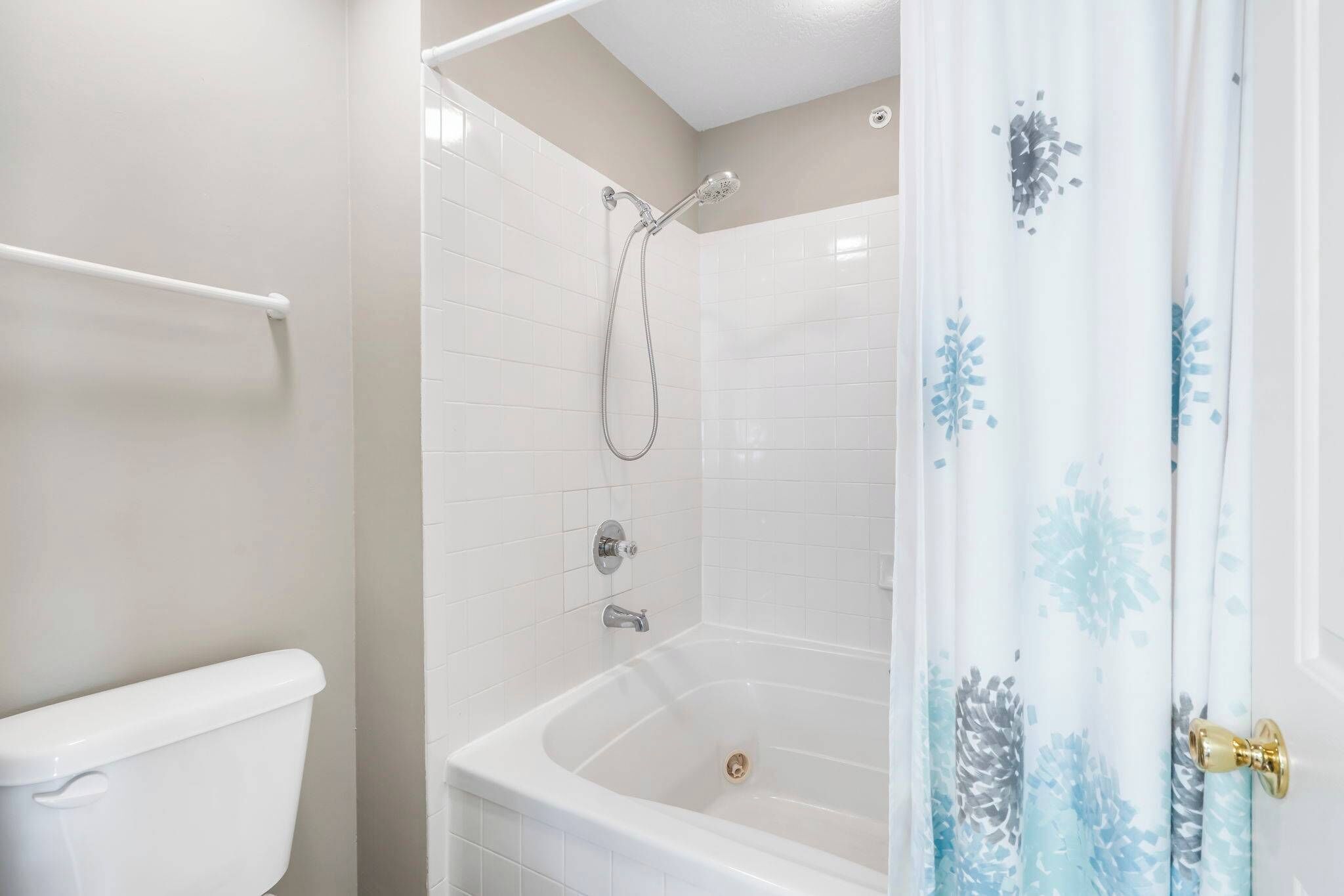 A bathroom with a white toilet, a bathtub with a showerhead, and a white tiled wall.