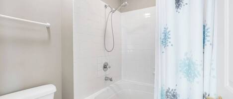 A bathroom with a white toilet, a bathtub with a showerhead, and a white tiled wall.
