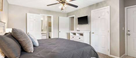 A bedroom with a bed, ceiling fan, white doors, and a television on the wall.