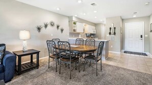 A dining area with a round table and six chairs, a small side table with a lamp, and a kitchen in the background. - Golf View Escape - Holiday Hills Branson - Golf - Outdoor Pools (Branson)
