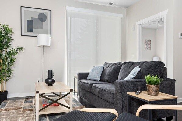 Un salon moderne avec un canapé gris, une petite table en bois, une lampe sur pied et une plante en pot.