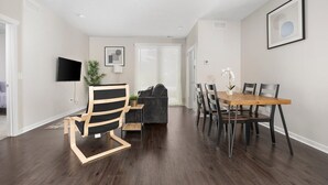 A modern living room with a dark wood floor, a black and white chair, a grey sofa, and a dining table with chairs. - 1st Floor Condo | 2 Queen Beds + TART Trail (Traverse City)