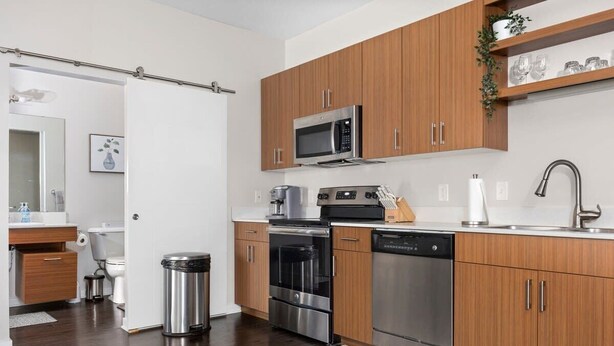 A modern kitchen with wooden cabinets, stainless steel appliances, and a white countertop. - 1st Floor Condo | 2 Queen Beds + TART Trail (Traverse City)