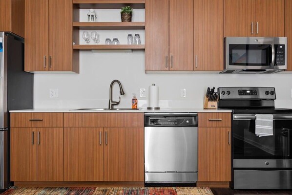 A modern kitchen with wooden cabinets, stainless steel appliances, and a built-in microwave.