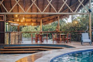 Uma área de piscina externa com espreguiçadeiras de madeira e uma estrutura de telhado de palha.
