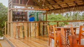 Un espace bar extérieur doté d’une structure en bois, d’un comptoir avec des bouteilles et de sièges.