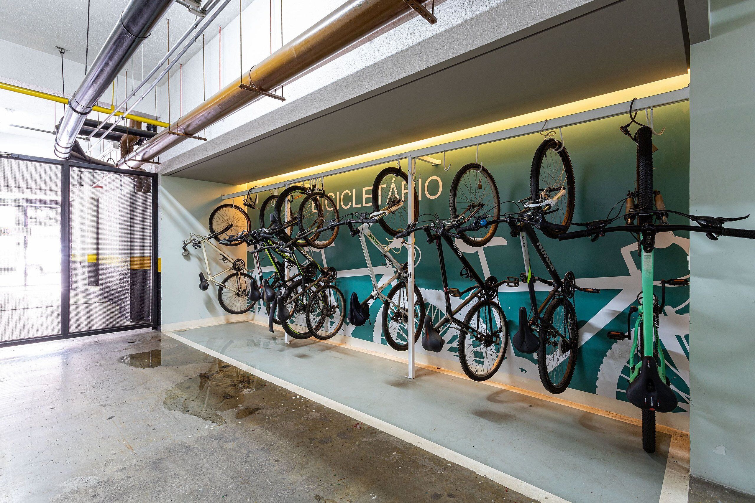A bike rental station with multiple bicycles mounted on a wall, a concrete floor, and a view of the street outside.