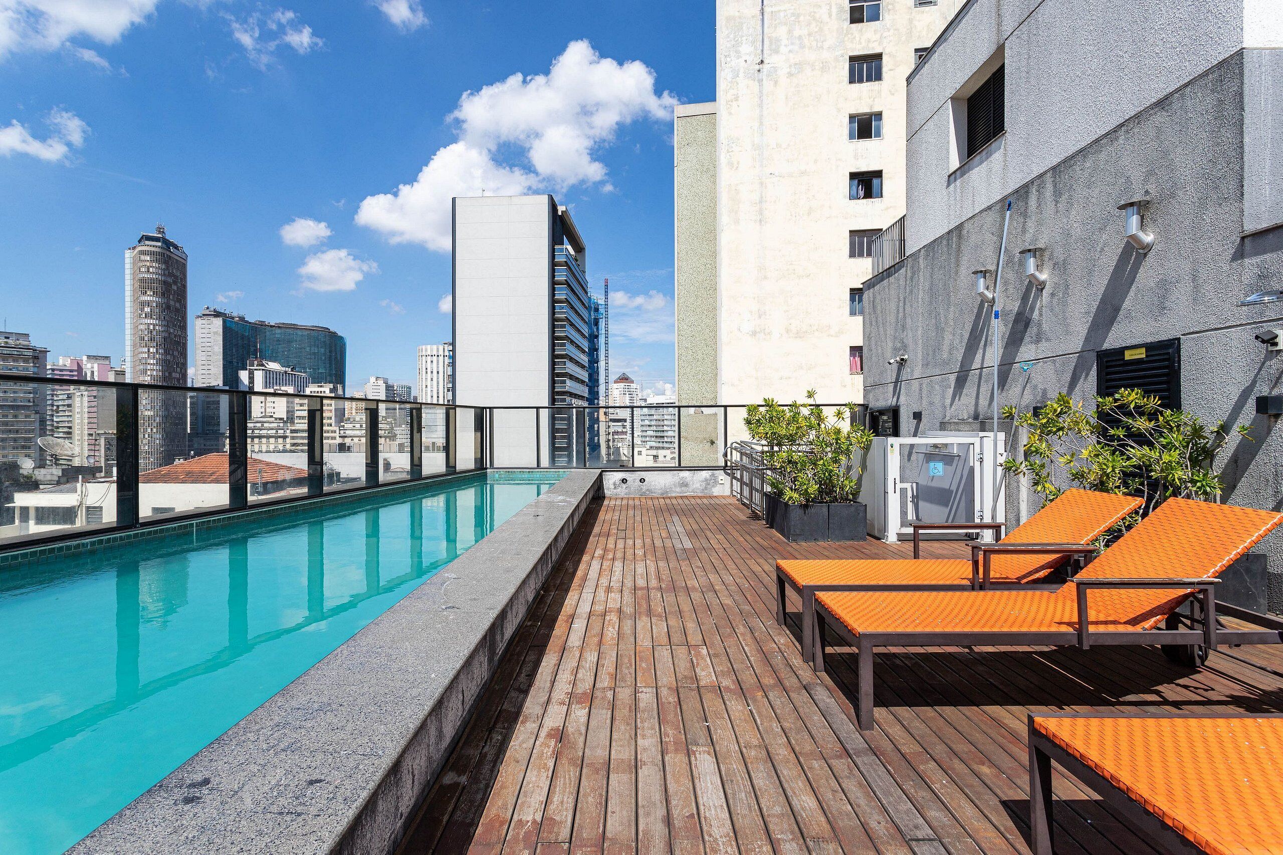 Ein Poolbereich auf dem Dach mit einer Holzterrasse, Liegestühlen und Blick auf die Stadt.