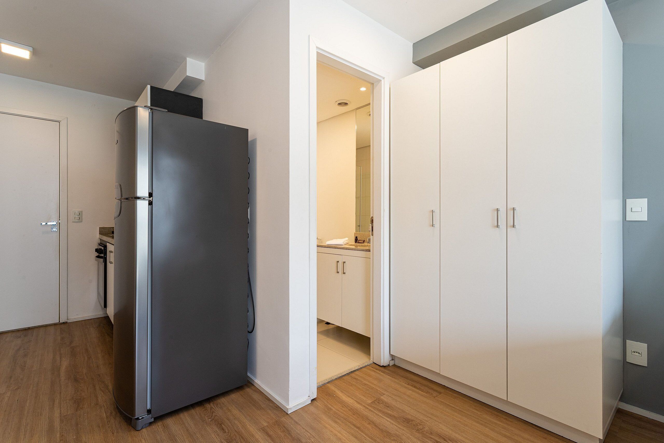 Une cuisine moderne avec un réfrigérateur en acier inoxydable, des armoires blanches et un plancher en bois.
